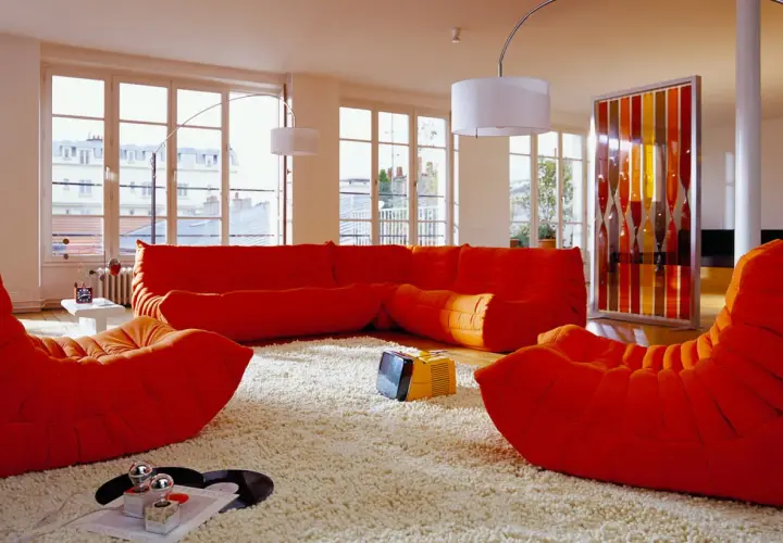 Salon aux couleurs vives, mobilier années 70 caractéristiques : canapé orange, fauteuils Togo, tapis shaggy, écran décoratif coloré.