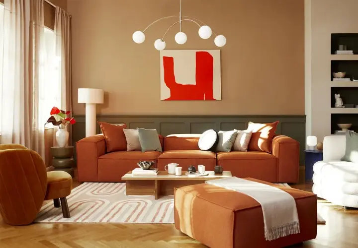 Salon cosy aux tons terreux. Un canapé orange vif, des coussins doux et une peinture abstraite rouge créent une ambiance chaleureuse. La **couleur chaude peinture** domine, invitant à la détente.