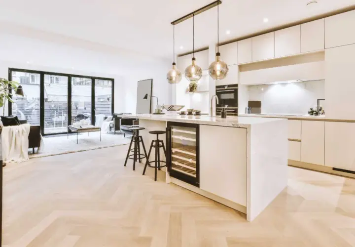 Éclairage cuisine ouverte sur salon avec îlot central, cave à vin et tabourets. Lumière douce et moderne.