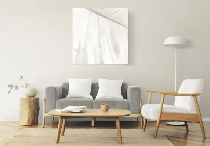 Salon à la décoration minimaliste : canapé gris, fauteuil blanc, table basse en bois, tableau abstrait et lampe sur pied.