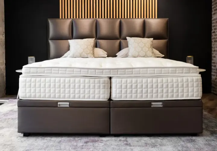 Un lit moderne avec un sommier capitonné marron, idéal pour poser un sommier à lattes. Le matelas est blanc et deux coussins décoratifs sont présents.
