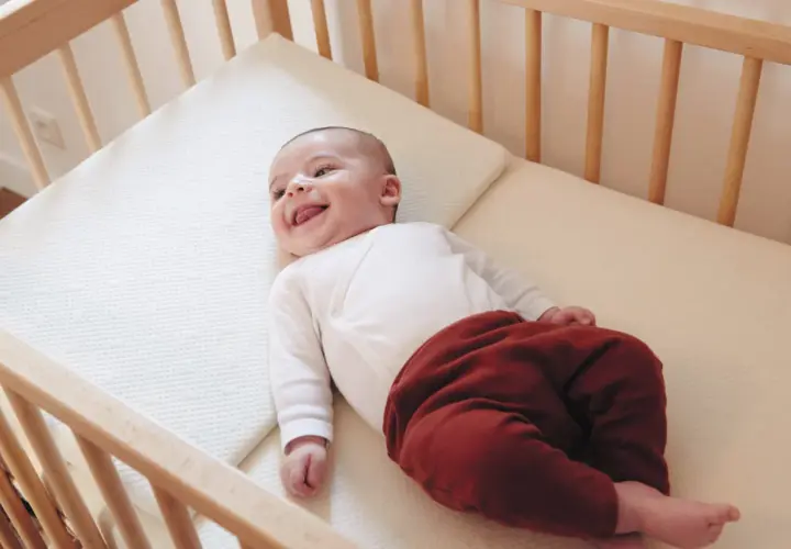 Un bébé souriant dans un lit en bois. Quel lit pour bébé est le plus confortable ? Ce matelas semble parfait pour des siestes douces.