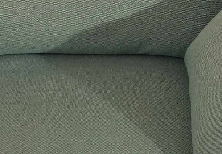 Gros plan sur le tissu texturé d'un canapé vert. Une assise de canapé qui glisse, créant une ombre douce.