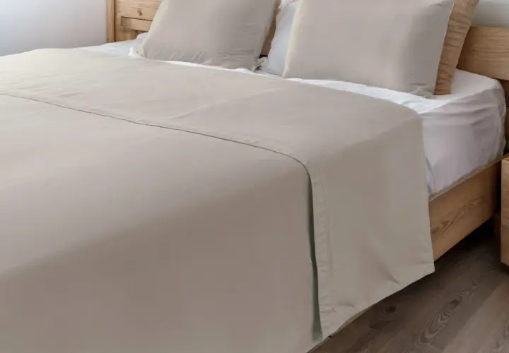 Un drap de lit beige, taille 140x190, est posé sur un lit en bois avec des oreillers assortis.