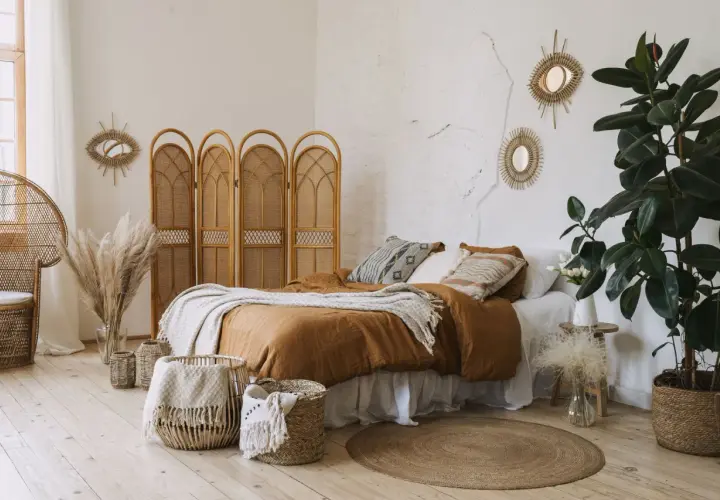 Une chambre d'amis cosy avec un lit douillet, des paniers en osier, des miroirs soleil et une plante verte luxuriante.