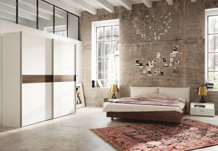 Chambre moderne avec grand placard blanc, lit bas, tapis oriental et mur en béton. Une décoration murale de photos et une lampe originale complètent ce **feng shui chambre**.