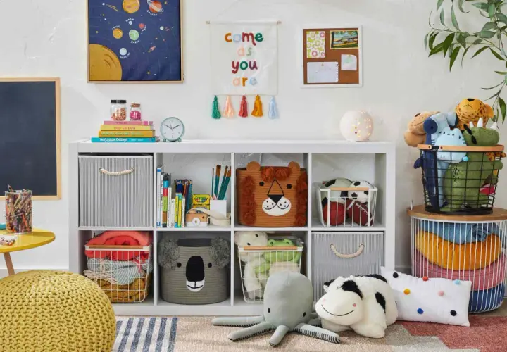 Idée petite chambre bébé : étagère blanche remplie de jouets, paniers animaux, coussins, et décorations murales colorées.