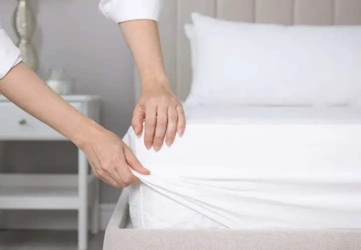Mains ajustant un drap housse blanc sur un matelas. La question est : quelle taille de drap housse pour un lit 160x200 ?