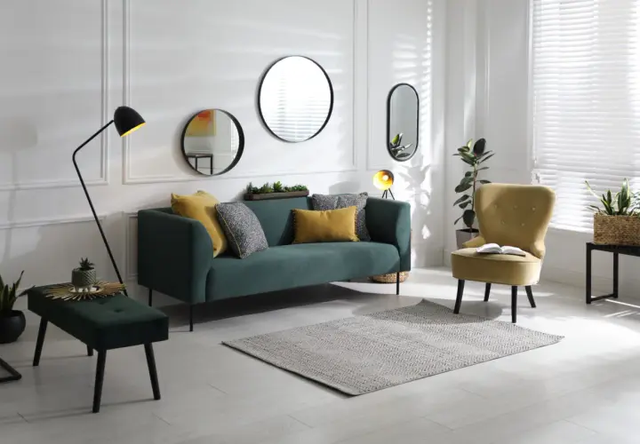 Un salon moderne avec un canapé vert, un fauteuil jaune et plusieurs miroirs derrière le canapé.
