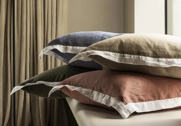 Pile de coussins aux couleurs douces, en matière drap de lin, avec des bordures blanches.
