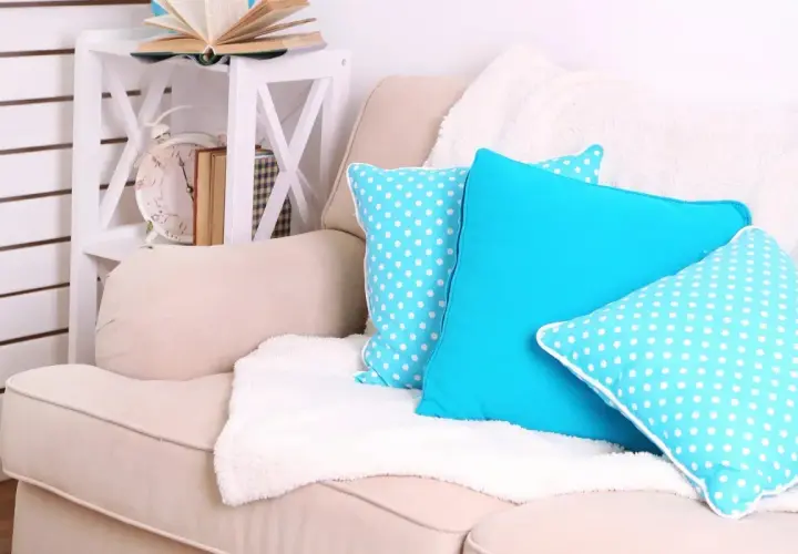 Un plaid blanc moelleux est disposé sur un canapé beige, orné de coussins bleus vifs et à pois. Idéal pour savoir comment disposer un plaid sur un canapé.