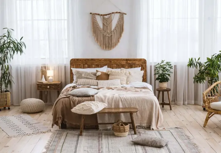 Chambre déco bohème avec un lit en bois, des coussins texturés, des plantes vertes et un macramé mural. Ambiance douce et naturelle.