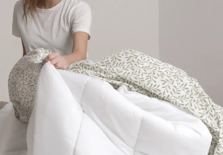 Une personne en t-shirt blanc commence à mettre la housse de couette à motifs feuilles sur une couette blanche.