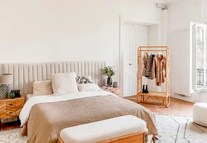 Chambre bohème scandinave avec lit douillet, table de chevet en bois, portant à vêtements en rotin et fenêtre lumineuse.