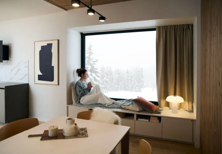 Un coin lecture scandinave parfait pour admirer la neige. Une femme savoure une boisson chaude, enveloppée dans un plaid douillet.