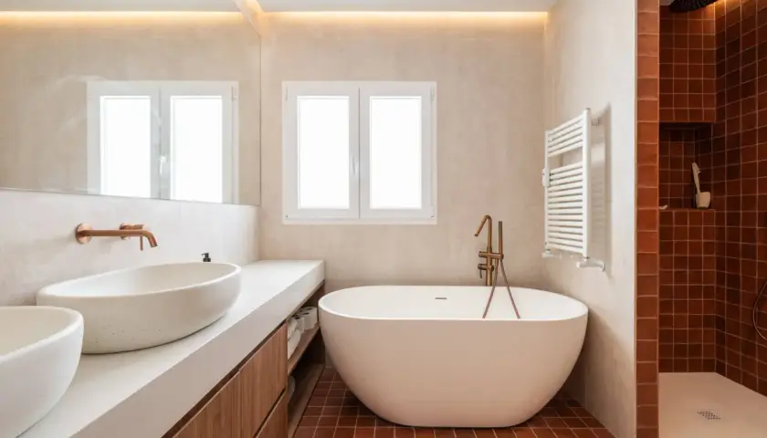 Salle de bain moderne avec baignoire îlot. L'éclairage indirect au plafond et la lumière naturelle par la fenêtre aident à comment éclairer une salle de bain.