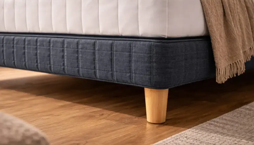 Un lit avec un sommier bleu foncé capitonné et des pieds en bois coniques. La hauteur du lit est celle d'un hauteur lit standard.