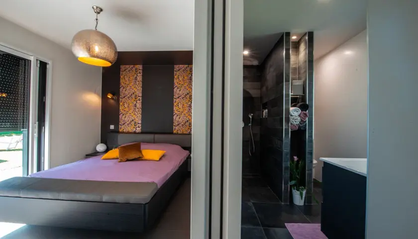 Chambre moderne avec lit violet et salle de bain attenante. La **taille suite parentale** est idéale pour un confort optimal.