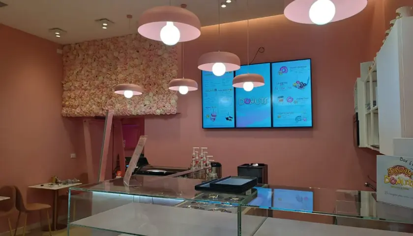 Cinq luminaires identiques, de couleur rose, éclairent un salon de thé aux murs ornés de fleurs roses.