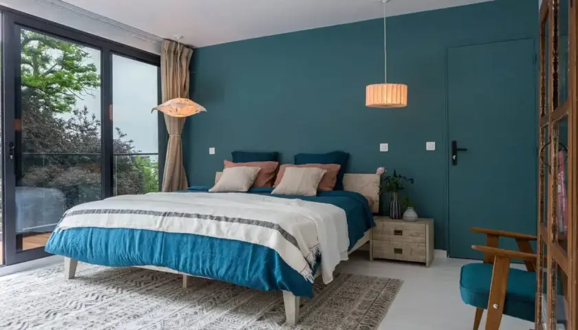 Chambre bleu nuit et bois, avec un grand lit douillet, une fenêtre donnant sur la verdure et une touche de naturel.