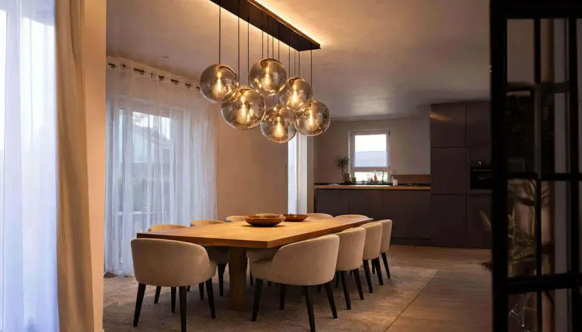Une table à manger moderne avec des chaises confortables, éclairée par un lustre sphérique, une vraie tendance luminaire.