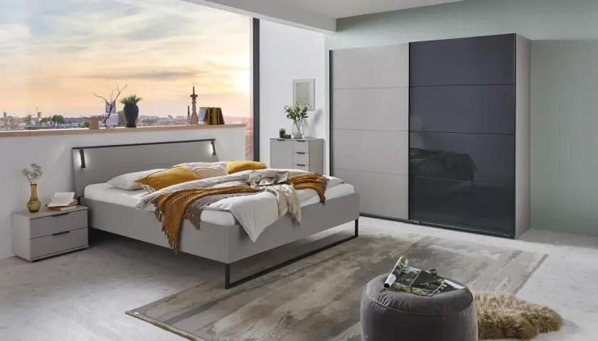 Chambre grise cocooning avec lit douillet, armoire moderne et vue sur la ville au coucher du soleil.