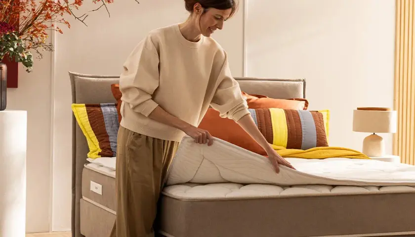 Une femme ajuste un surmatelas sur un lit. Idéal pour savoir comment surélever un lit et améliorer le confort.