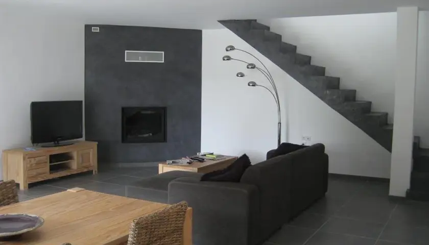 Salon moderne avec mur noir autour de la cheminée, sol gris foncé, escalier en béton, canapé marron et meuble TV en bois. Quelle couleur de mur avec un sol gris foncé ? Le noir contraste bien.
