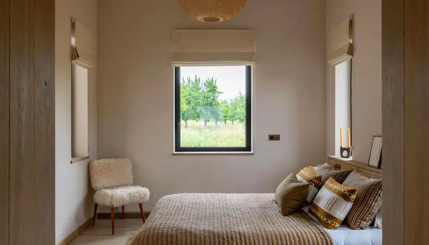 Une petite chambre parentale cosy avec un lit douillet, un fauteuil en peau de mouton et une vue sur la nature.