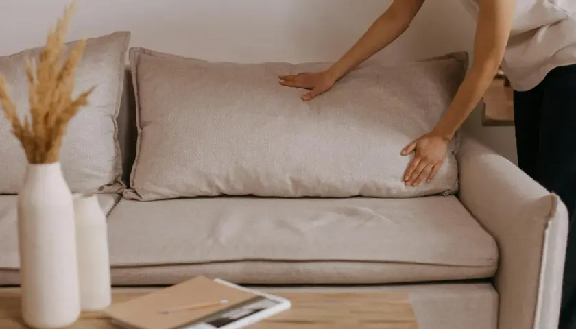 Comment faire pour le rembourrage canapé coussins avachis ? Une main ajuste un coussin pour lui redonner sa forme.