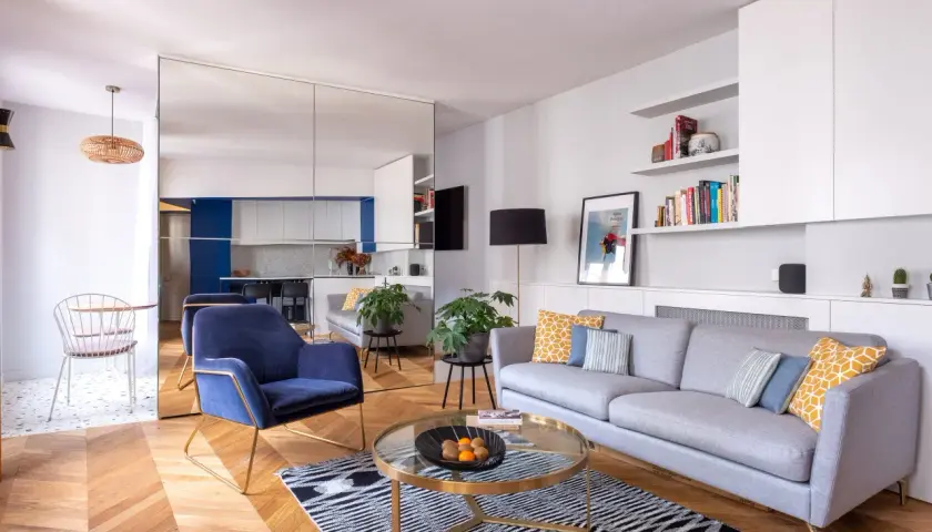 Salon moderne avec canapé gris, fauteuil bleu, table basse ronde et parquet. La deco petit appartement moderne est lumineuse et élégante.