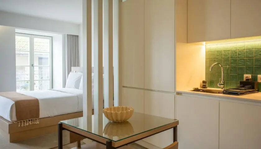 Un studio aménagé pour créer une chambre et une cuisine fonctionnelle. Un lit douillet fait face à une fenêtre, tandis qu'une kitchenette moderne est séparée par des cloisons.