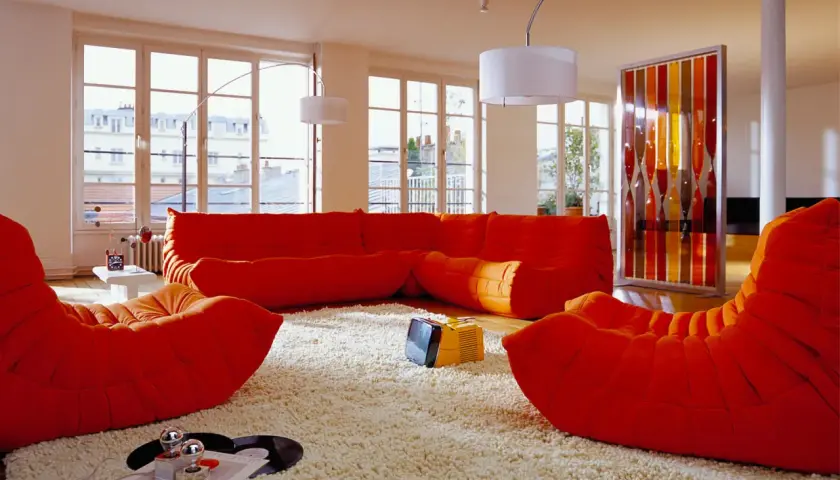 Salon aux couleurs vives, mobilier années 70 caractéristiques : canapé orange, fauteuils Togo, tapis shaggy, écran décoratif coloré.