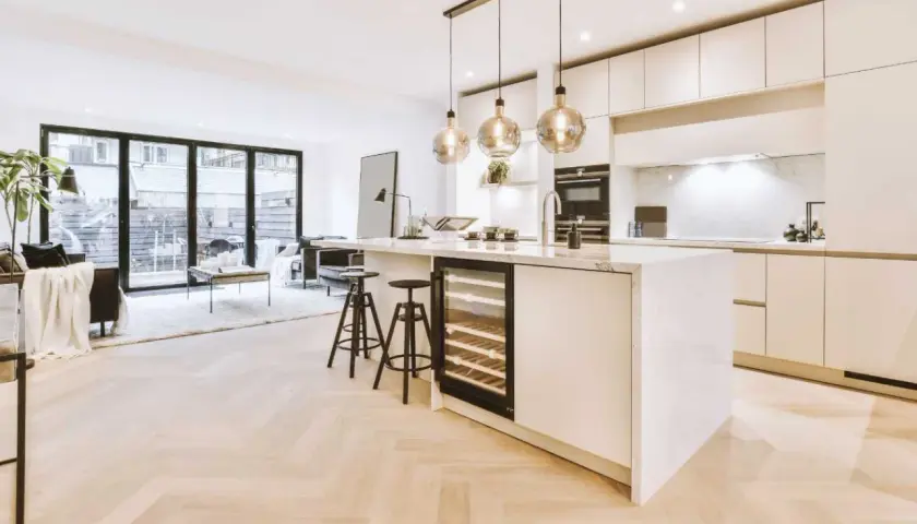 Éclairage cuisine ouverte sur salon avec îlot central, cave à vin et tabourets. Lumière douce et moderne.
