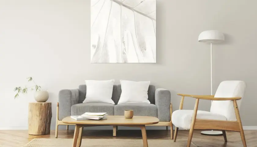 Salon à la décoration minimaliste : canapé gris, fauteuil blanc, table basse en bois, tableau abstrait et lampe sur pied.
