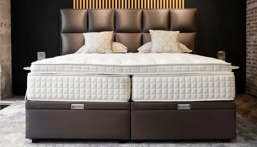 Un lit moderne avec un sommier capitonné marron, idéal pour poser un sommier à lattes. Le matelas est blanc et deux coussins décoratifs sont présents.