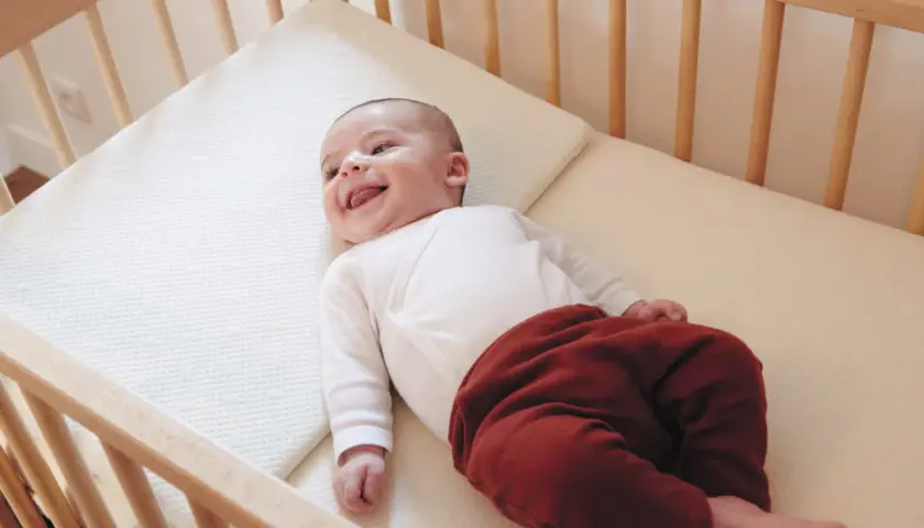 Un bébé souriant dans un lit en bois. Quel lit pour bébé est le plus confortable ? Ce matelas semble parfait pour des siestes douces.
