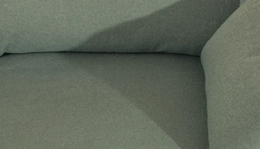 Gros plan sur le tissu texturé d'un canapé vert. Une assise de canapé qui glisse, créant une ombre douce.