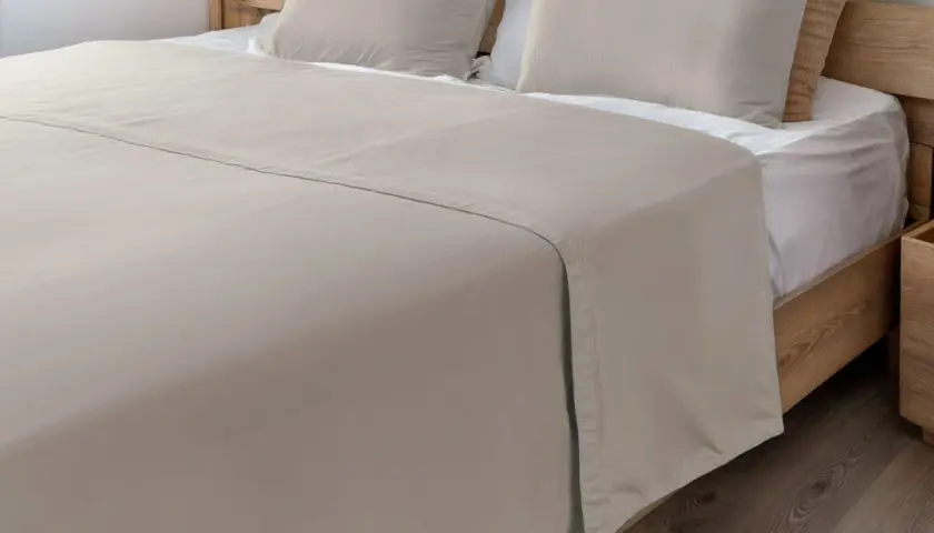 Un drap de lit beige, taille 140x190, est posé sur un lit en bois avec des oreillers assortis.