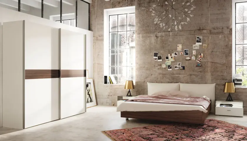 Chambre moderne avec grand placard blanc, lit bas, tapis oriental et mur en béton. Une décoration murale de photos et une lampe originale complètent ce **feng shui chambre**.