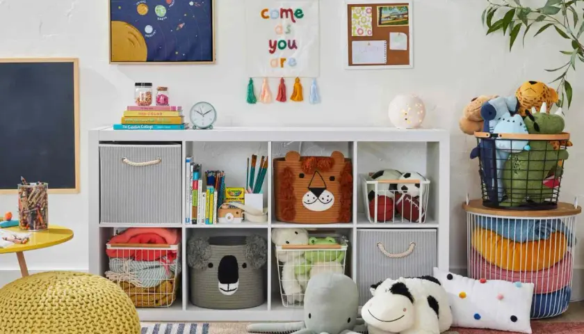 Idée petite chambre bébé : étagère blanche remplie de jouets, paniers animaux, coussins, et décorations murales colorées.