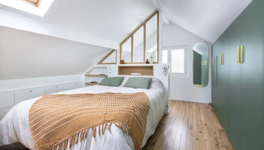 Suite parentale sous comble avec salle de bain et dressing. Un lit douillet, des rangements intégrés et une verrière style verrière d'atelier apportent charme et fonctionnalité.