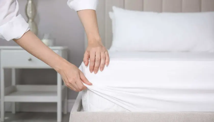 Mains ajustant un drap housse blanc sur un matelas. La question est : quelle taille de drap housse pour un lit 160x200 ?