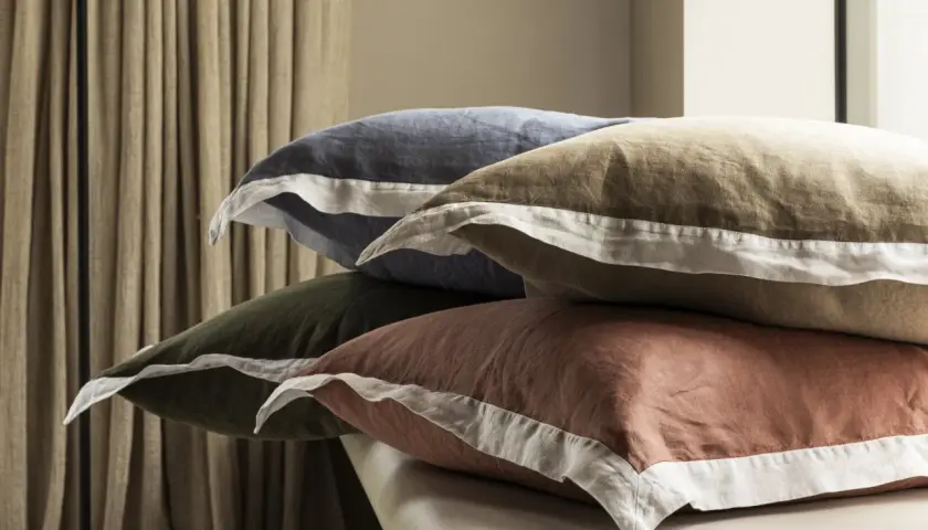 Pile de coussins aux couleurs douces, en matière drap de lin, avec des bordures blanches.