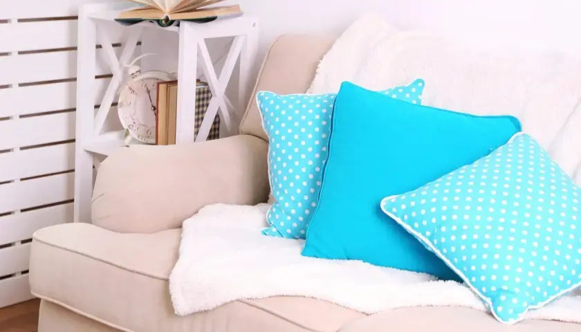 Un plaid blanc moelleux est disposé sur un canapé beige, orné de coussins bleus vifs et à pois. Idéal pour savoir comment disposer un plaid sur un canapé.