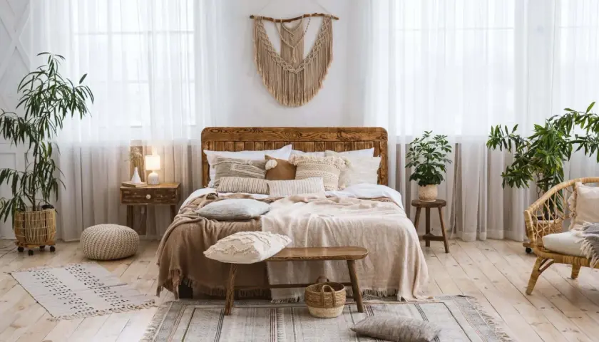 Chambre déco bohème avec un lit en bois, des coussins texturés, des plantes vertes et un macramé mural. Ambiance douce et naturelle.