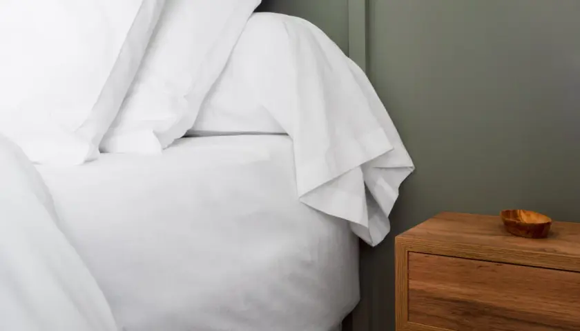 Un lit blanc immaculé avec un drap housse bien ajusté, prêt pour une nuit paisible. C'est quoi un drap housse ? C'est ce qui protège votre matelas.
