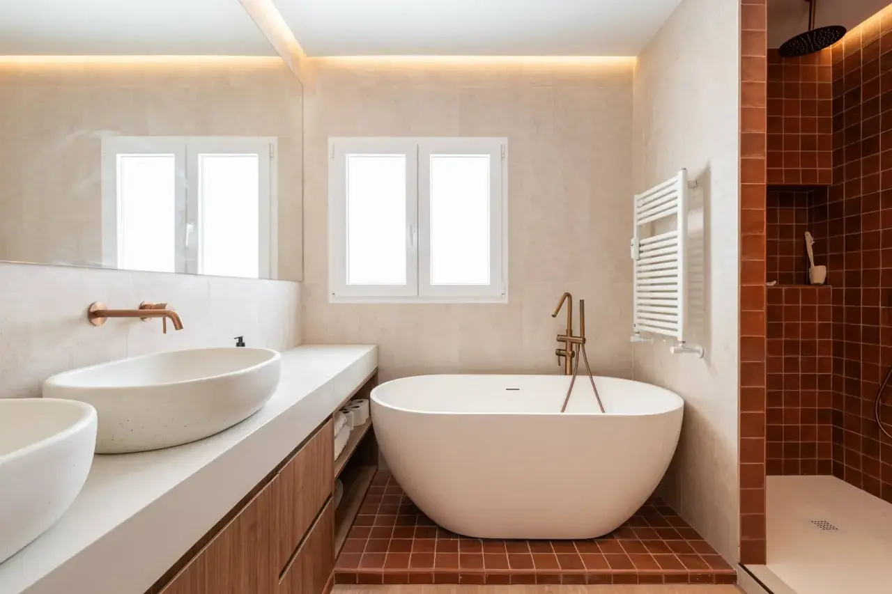 Salle de bain moderne avec baignoire îlot. L'éclairage indirect au plafond et la lumière naturelle par la fenêtre aident à comment éclairer une salle de bain.
