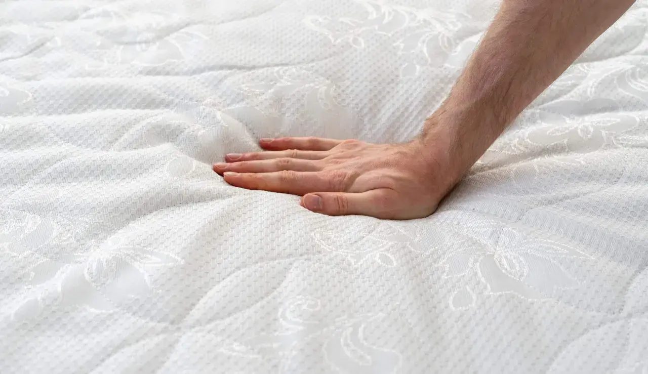 Main d'une personne appuyant sur un matelas blanc, créant une empreinte. Est-ce normal que mon matelas neuf se creuse ?