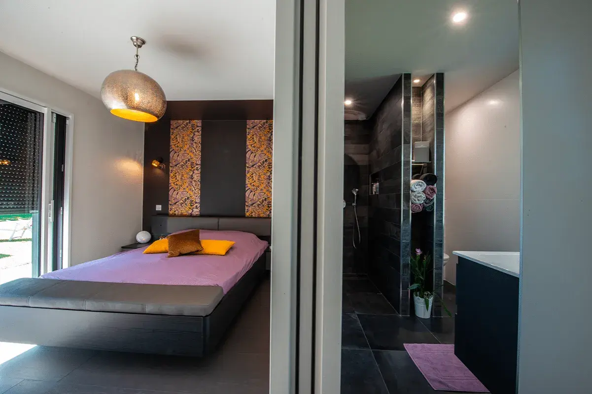 Chambre moderne avec lit violet et salle de bain attenante. La **taille suite parentale** est idéale pour un confort optimal.